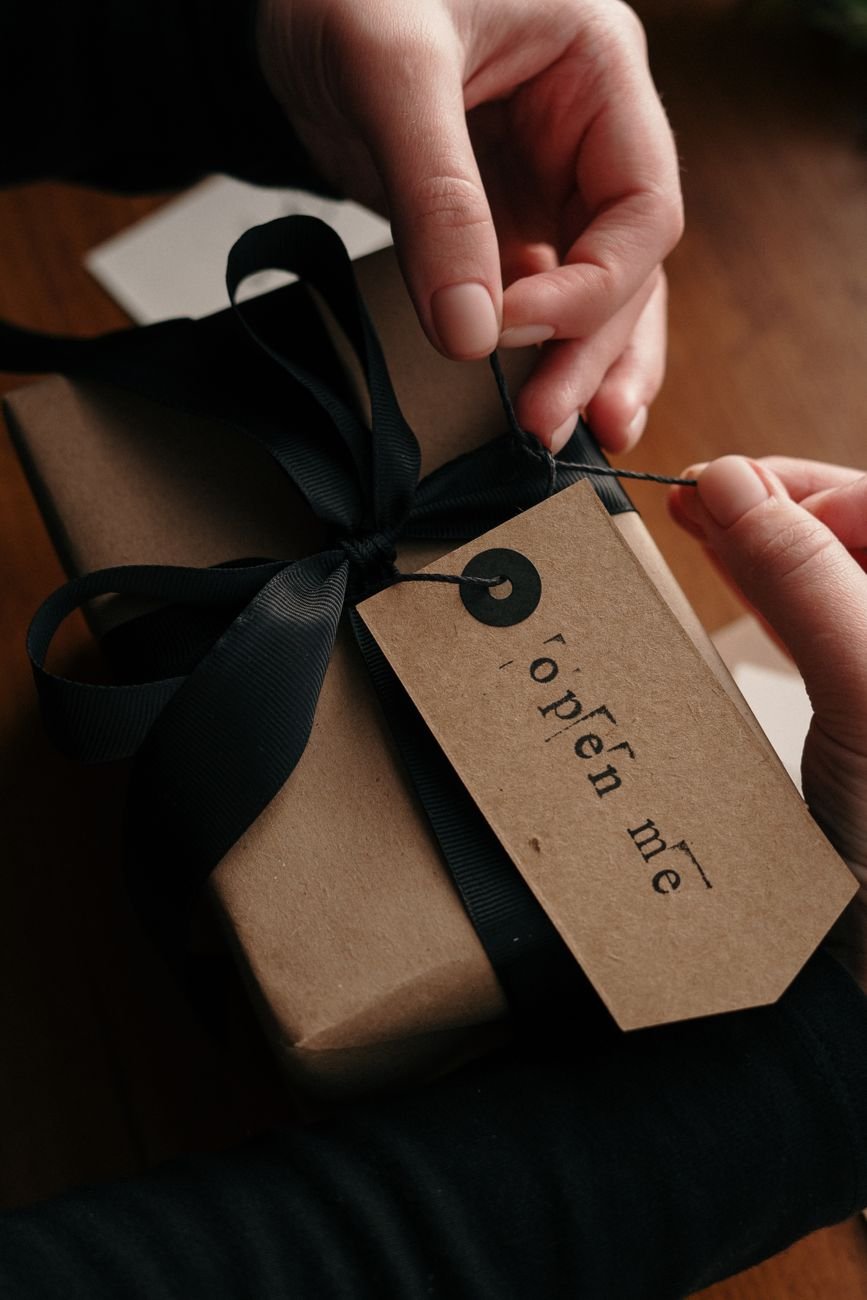 Hands unwrapping a gift box with an Open Me tag — the unboxing moment